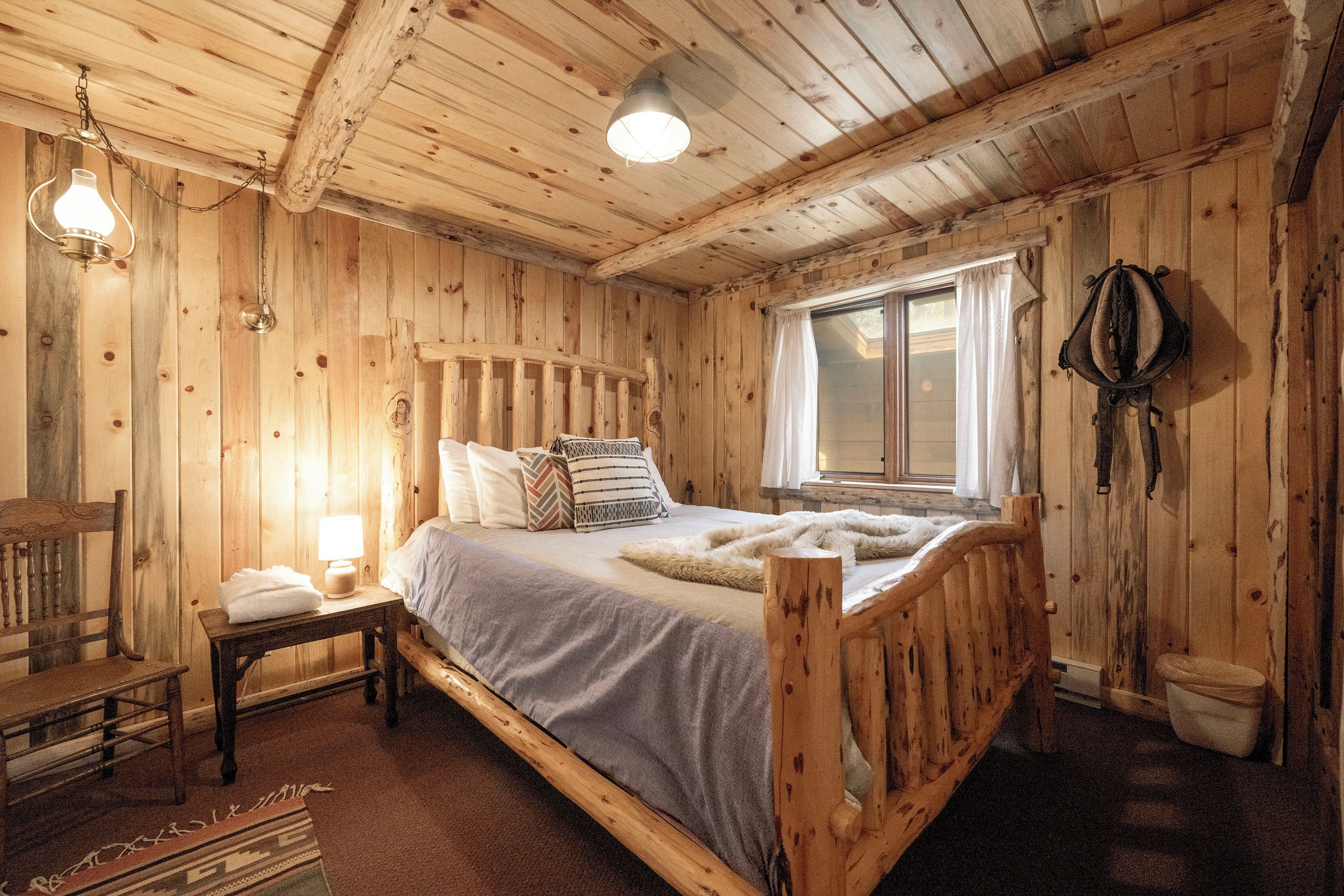 A wooden cabin bedroom with a bed, bedside table, lamp, and a window.