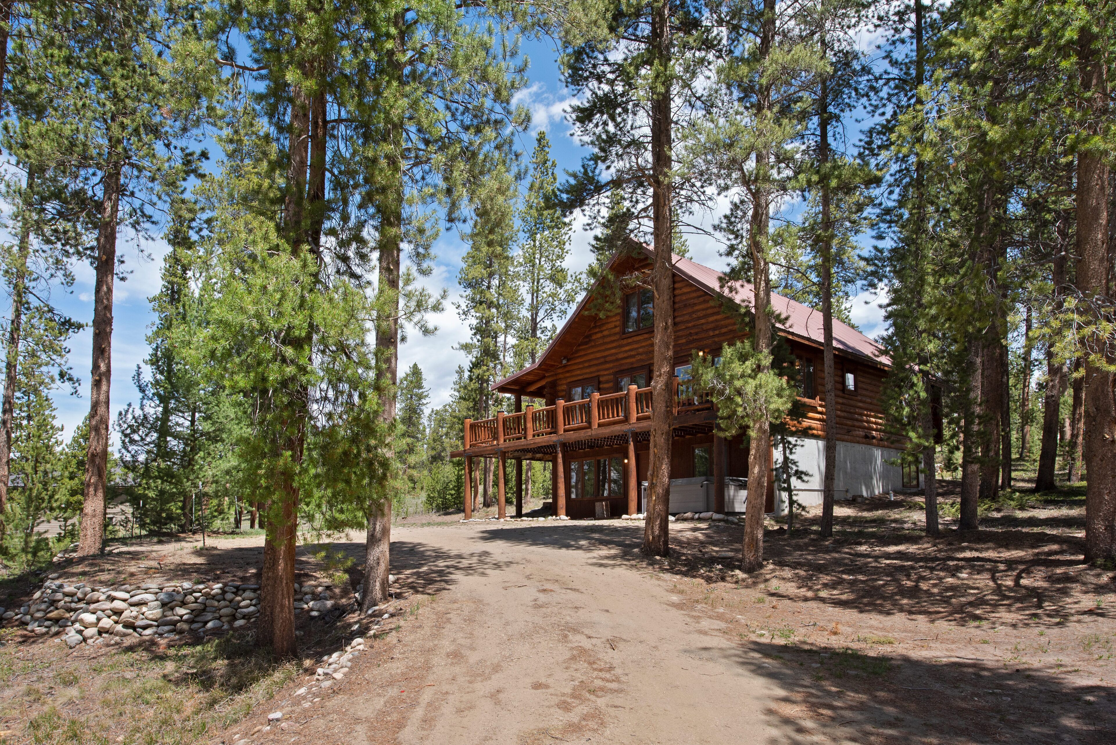A log cabin with a balcony, surrounded by tall pine trees.