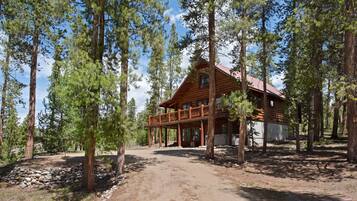A log cabin with a balcony, surrounded by tall pine trees.