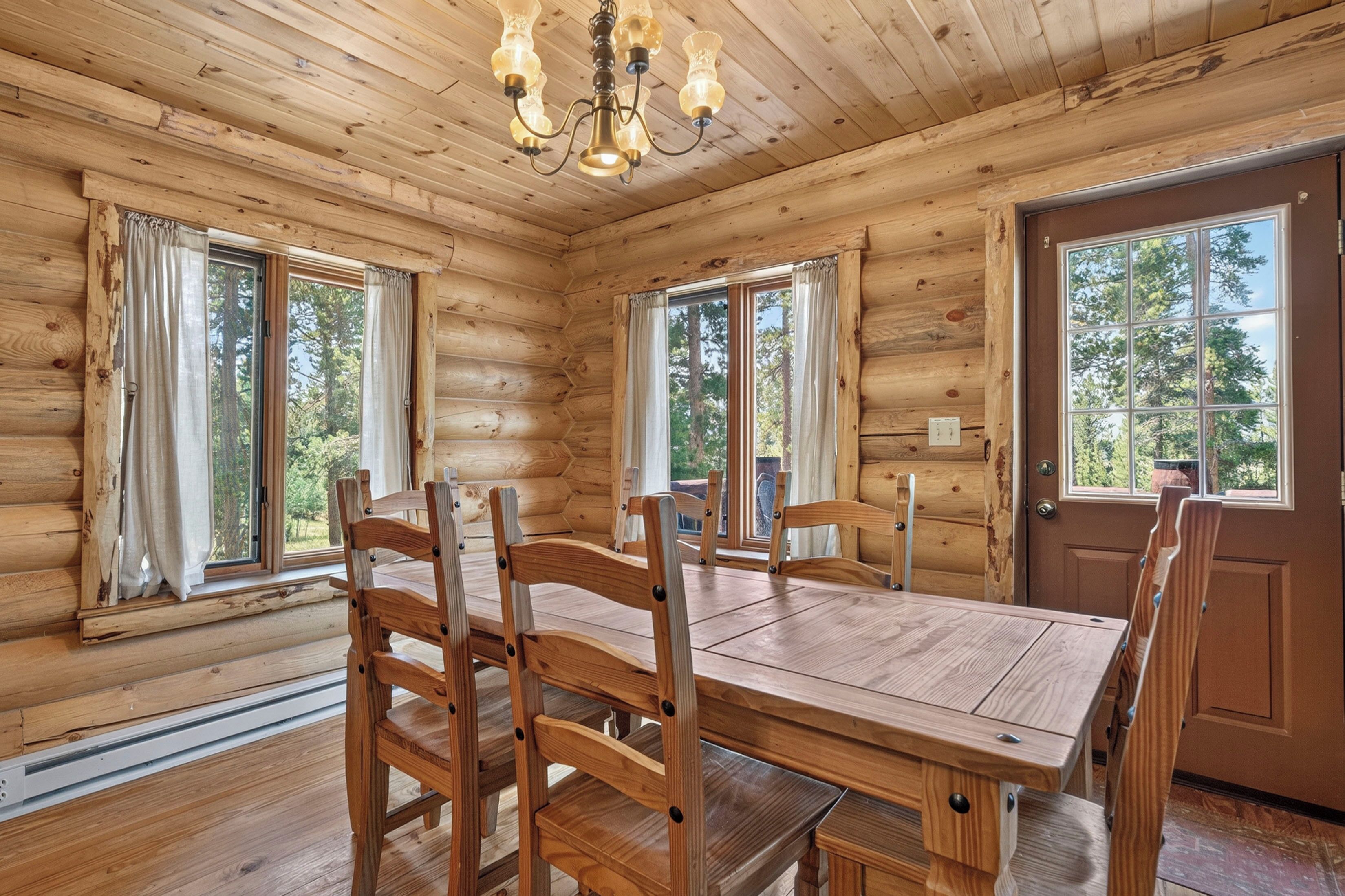 L’intérieur d’une cabane en rondins, avec une table et des chaises en bois, de grandes fenêtres et un lustre.
