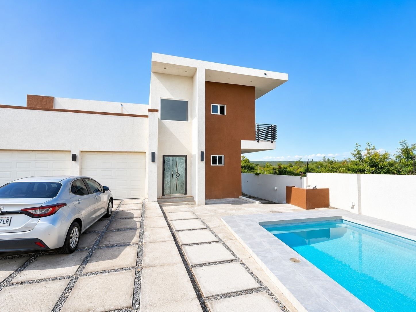 Et moderne hus med to etager, en swimmingpool, en bil på indkørslen og en klar blå himmel.