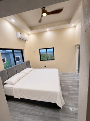 Ein Schlafzimmer mit einem Bett, Deckenventilator, Klimaanlage, einem Fenster mit Ausblick und einer Tür.