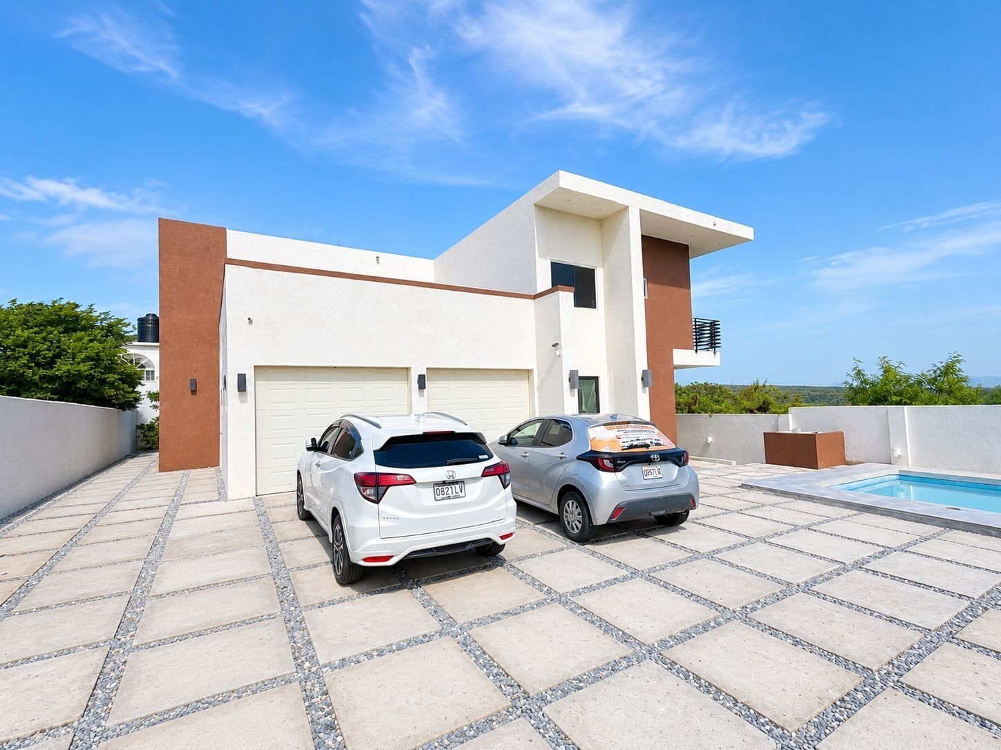 A modern two-story house with a garage, two parked cars, and a swimming pool.