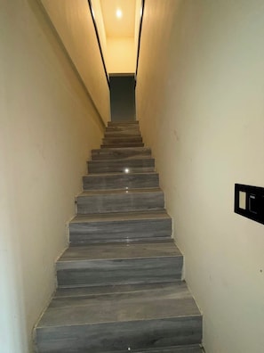 A straight, narrow stairway with a light fixture at the top and a wall-mounted switch on the right. -     Relax in Style  Modern Apartment with Balcony Overlooking the Pool (Hellshire)