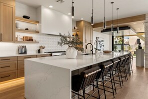 A modern kitchen with a marble island, bar stools, and pendant lighting. - Paradise Palace: Lagoon Front! Pool + Waterslide (St. George)