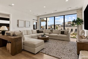 A modern living room with a sectional sofa, a coffee table, and a large window offering a view of the cityscape. - Paradise Palace: Lagoon Front! Pool + Waterslide (St. George)