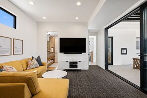 Ein modernes Wohnzimmer mit Sofa, Couchtisch, Flachbildfernseher und einem großen Fenster.