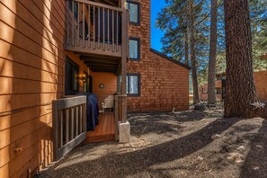 A wooden cabin with a balcony, a covered outdoor seating area, and a view of a forested area.