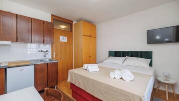 Habitación de hotel compacta con kitchenette, una cama y toallas ordenadas, televisión y una pequeña mesita.