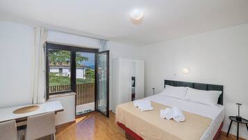 Habitación de hotel con cama, escritorio, silla, balcón con vistas y puerta que da a otra habitación.