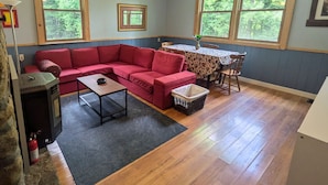 Ein gemütliches Wohnzimmer mit einem roten Ecksofa, einem kleinen Tisch, einem Deckenventilator und großen Fenstern.