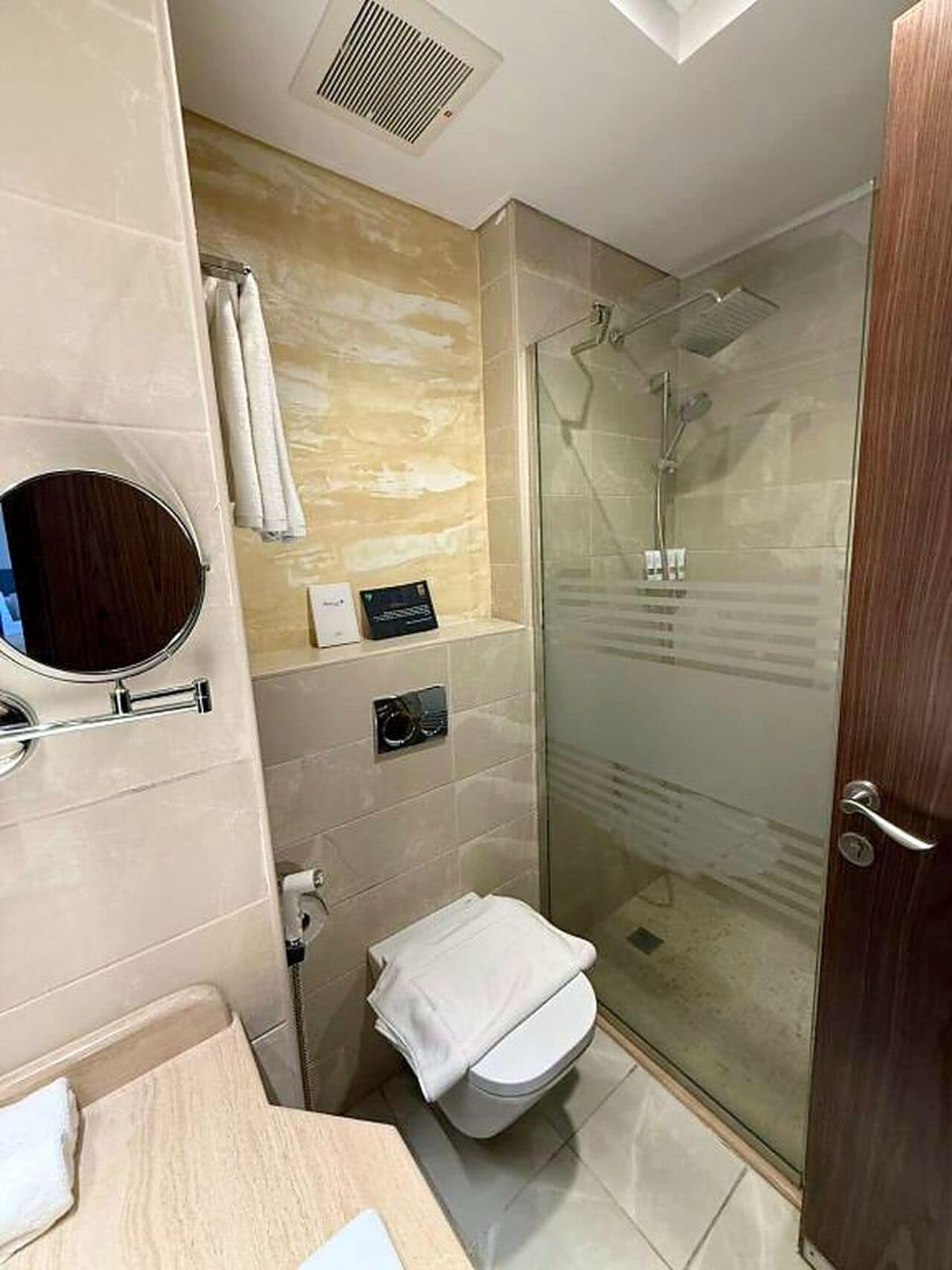 Un baño moderno con ducha envuelta en vidrio, inodoro, lavamanos con espejo y toallero.