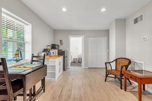 A modern kitchen with white cabinets, a wooden dining table, and a wicker chair. - ☀Quick Walk to Sunset Beach🌴Fun at Caddy's Treasure Island🐠Caddy's Cottage #1 (Treasure Island)