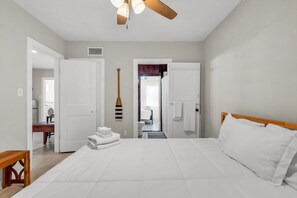 Un dormitorio con cama, ventilador de techo y vista al baño.