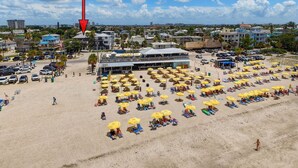 Een strand met veel ligbedden en parasols, een parkeerplaats en een gebouw met een plat dak.