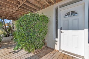 A wooden deck with a white door and a lush green bush. - ☀Quick Walk to Sunset Beach🌴Fun at Caddy's Treasure Island🐠Caddy's Cottage #1 (Treasure Island)