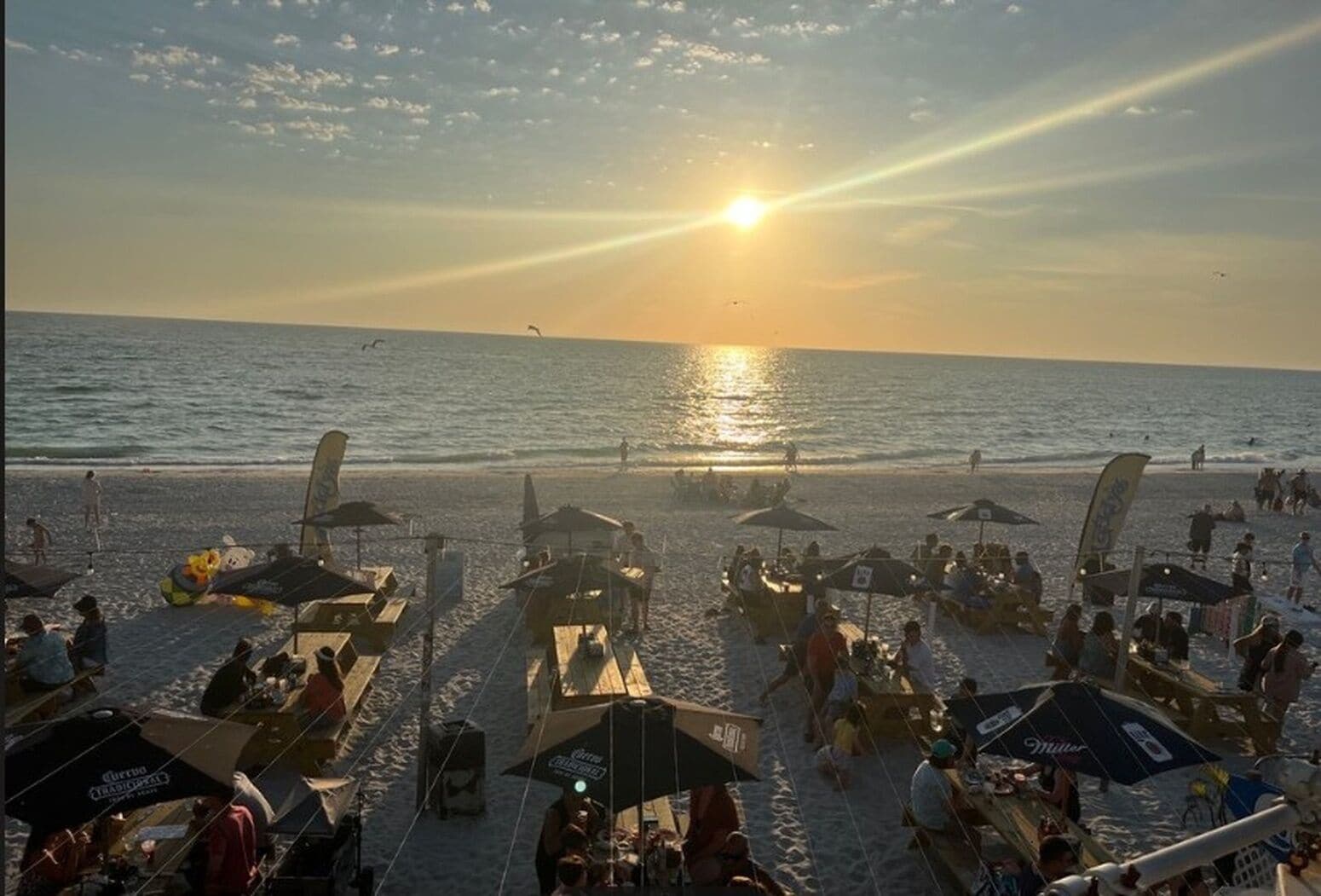 Ein Strand mit Sonnenschirmen, Menschen, einem Sonnenuntergang und dem Meer.