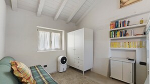 A room with a bed, a standing fan, a wardrobe, a bookshelf, and a window with curtains.