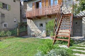 A rustic building with a wooden balcony, a metal ladder, and a small garden area with plants and outdoor furniture. - Holiday home 'Agnese' with lake view, private terrace and Wi-Fi (Pradello)