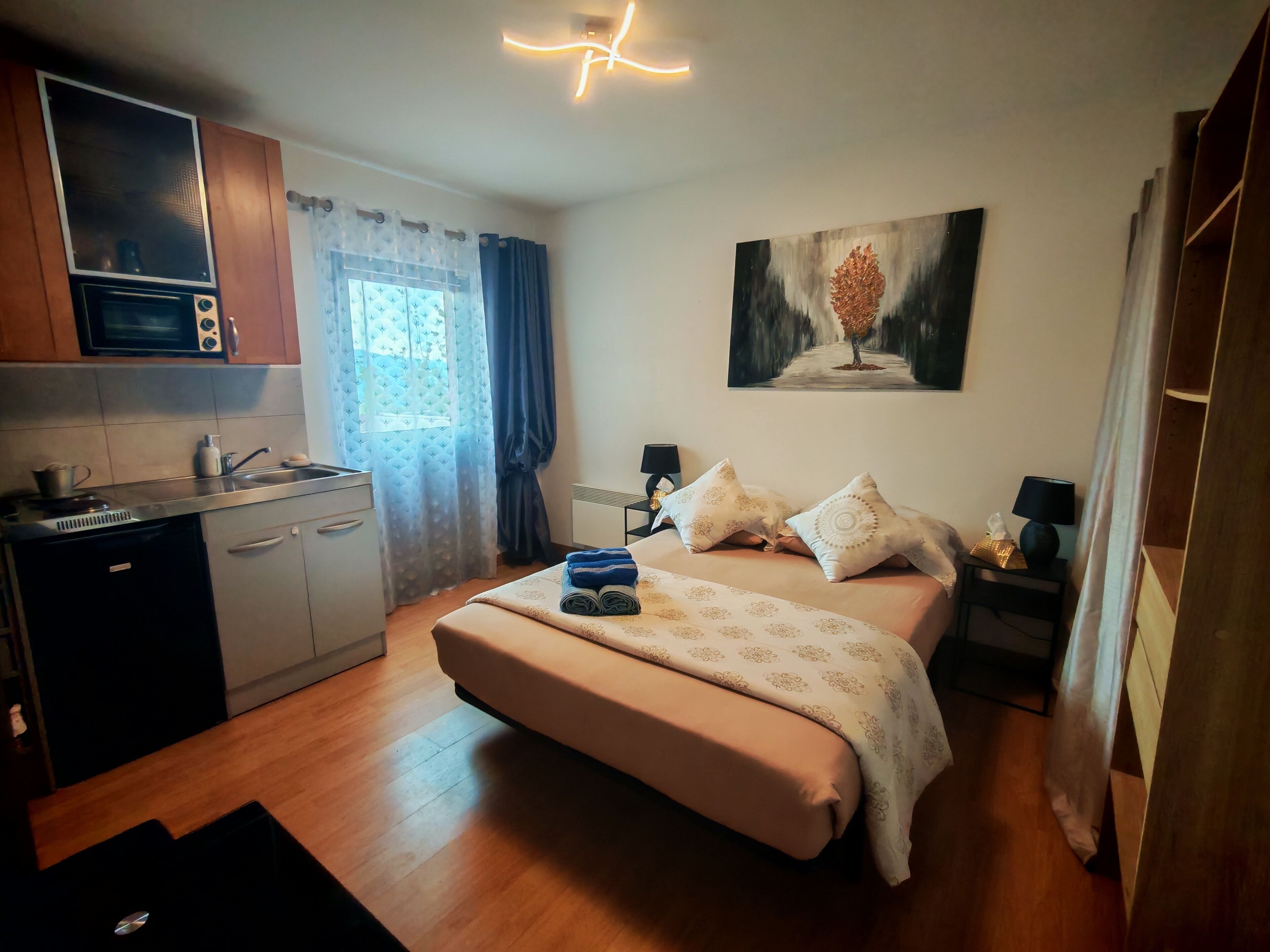 Ein Schlafzimmer mit einem Bett, Nachttischen, einem Gemälde und einer Küchenzeile inklusive Mikrowelle.