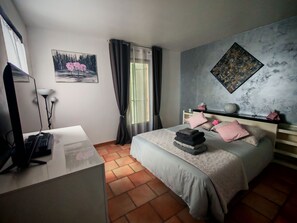 Un dormitori amb llit, escriptori, ordinador, finestra amb cortines i obra d'art a les parets.