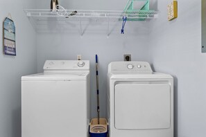 Ein Waschraum mit zwei weißen Waschmaschinen, einem Mop und einem Regal mit verschiedenen Gegenständen.