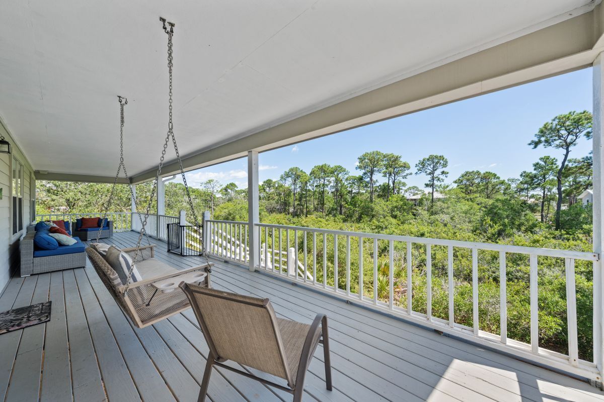 A covered porch with a swing chair, a sofa with cushions, and a view of a forested area.