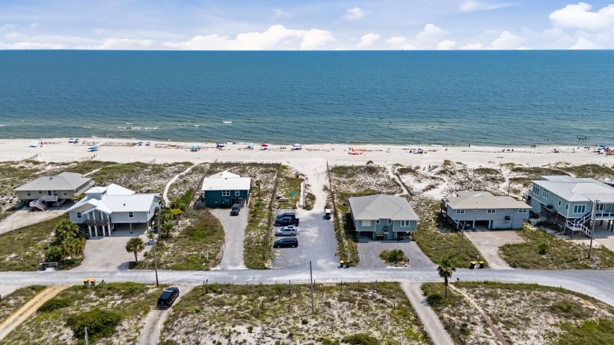 A coastal property with multiple buildings, a beach in the background, and a clear sky.