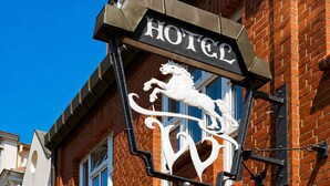 Segnaletica di un hotel con uno stemma raffigurante un leone, facciata in mattoni e cielo azzurro.