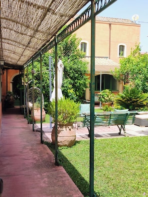 A covered walkway with potted plants, a bench, and a building with a tiled roof. - Campidhouse Luxury & Relax (Monserrato)