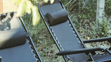 A row of lounge chairs with a mesh surface and a padded headrest, arranged outdoors with a fence and vegetation in the background.
