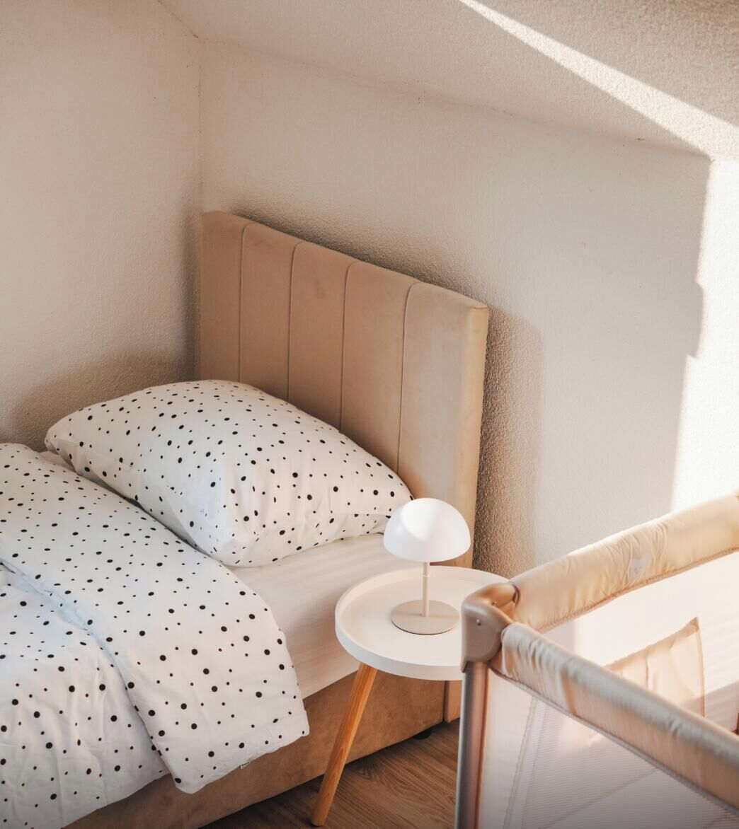 A bedroom with a bed, a bedside table with a lamp, and a view of the outside.