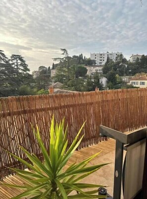 Ein Balkon mit Bambuszaun, einem Blumentopf und Blick auf Gebäude im Hintergrund.