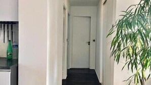 Kapea käytävä, jossa on tumma puulattia, valkoiset seinät ja oikealla puolella ruukussa oleva kasvi.