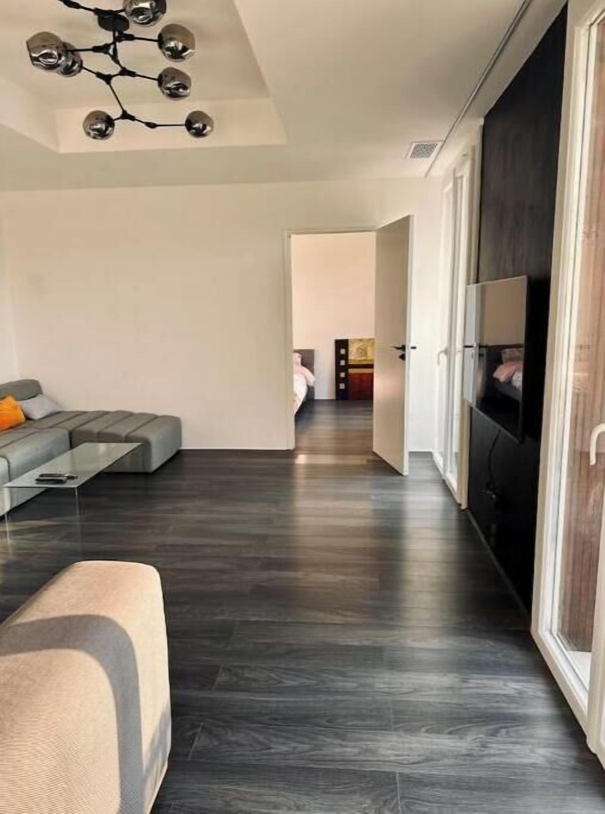 Ein modernes Wohnzimmer mit dunklem Holzboden, einem Ecksofa, einem Couchtisch und einem Fernseher auf einem Lowboard.