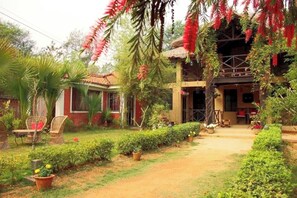 A house with a garden, a red brick exterior, and a thatched roof structure. - Jo'stel Eco Modern Earth (Bolpur)