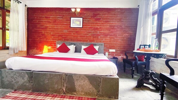 A room with a brick wall, a bed with white bedding and red pillows, a small table with a bottle, and a chair. - Jo'stel Eco Modern Earth (Bolpur)