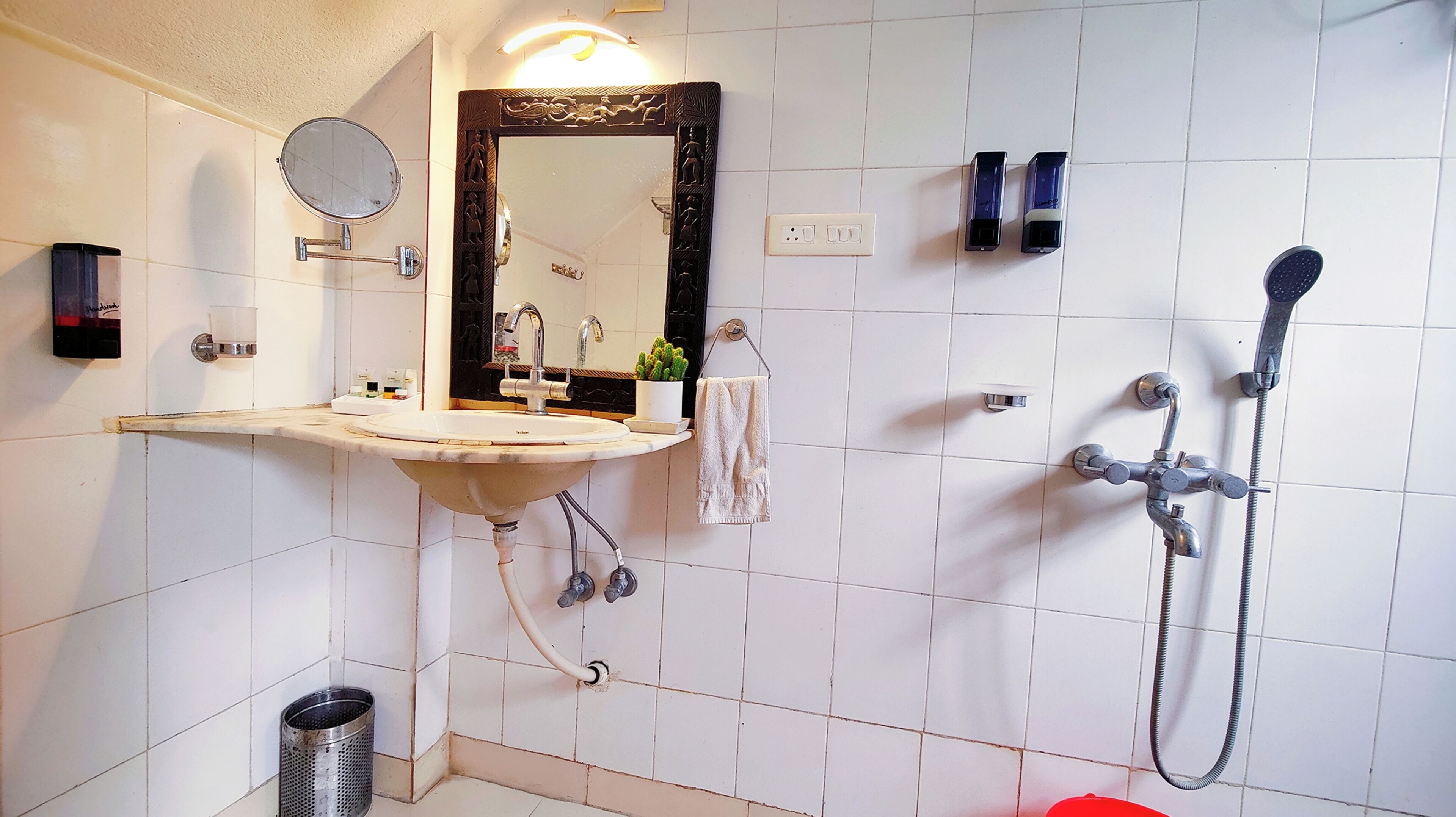 A bathroom with a sink, mirror, towel rack, shower, and a trash can.