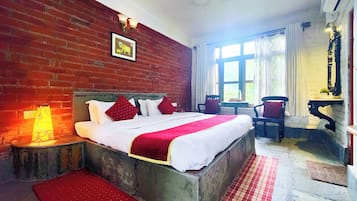 A hotel room with a brick wall, a bed with white bedding and red accents, a window with curtains, and a chair.