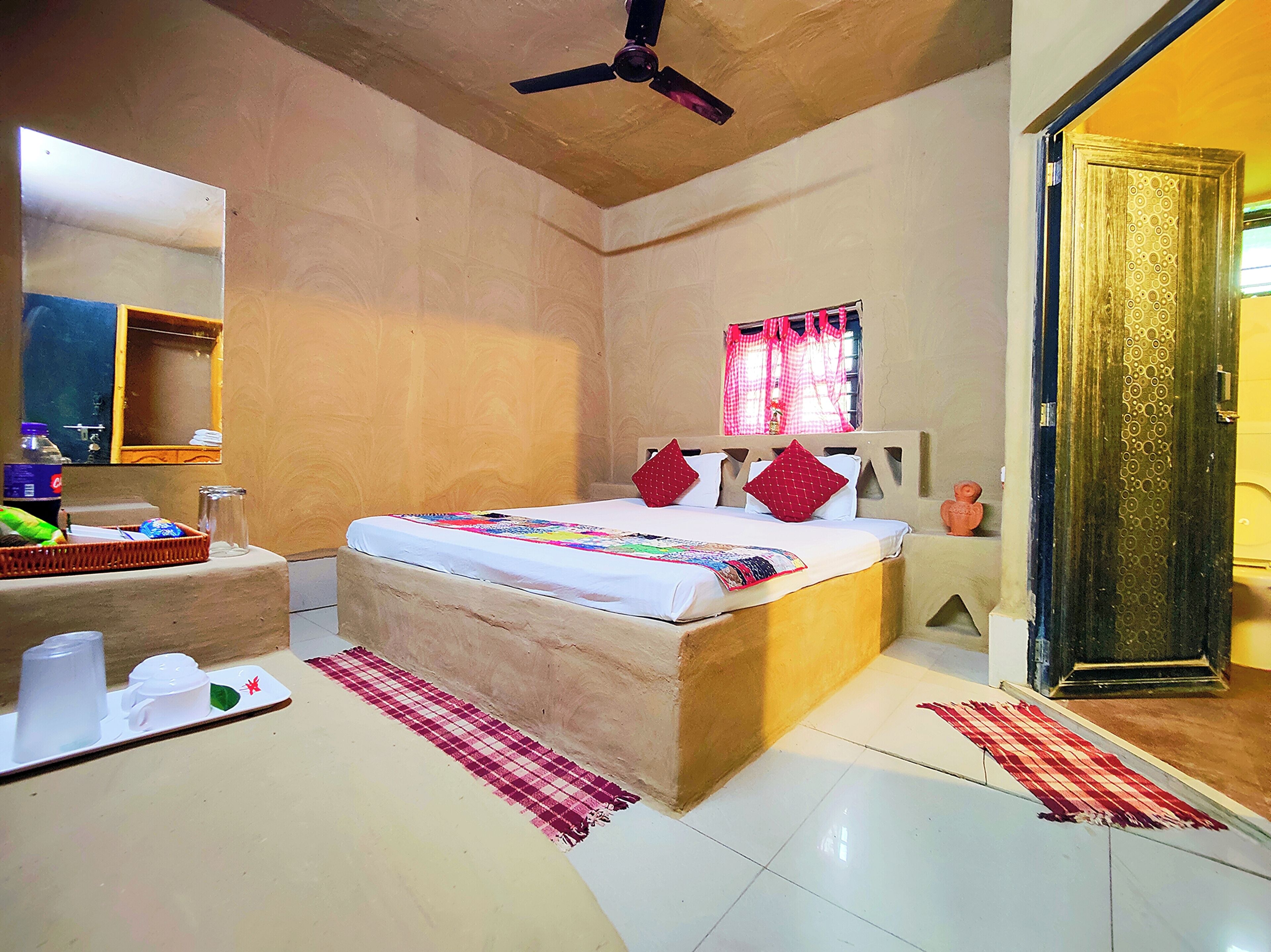 A bedroom with a bed, a ceiling fan, a window with curtains, a door, and a small table with items on it.