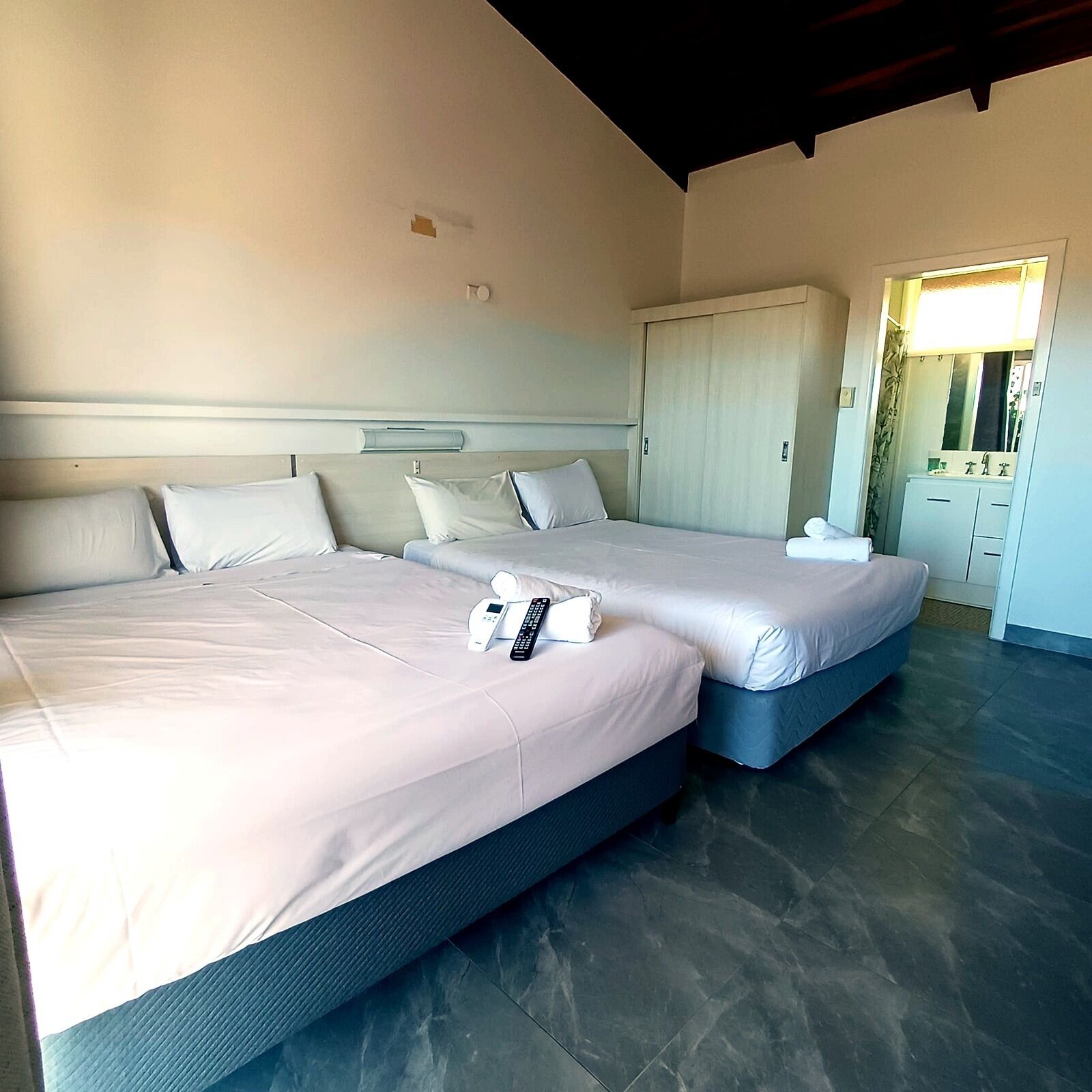 A hotel room with two beds, a wardrobe, and a bathroom visible through an open door.