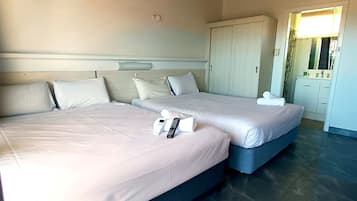 A hotel room with two beds, a wardrobe, and a bathroom visible through an open door.