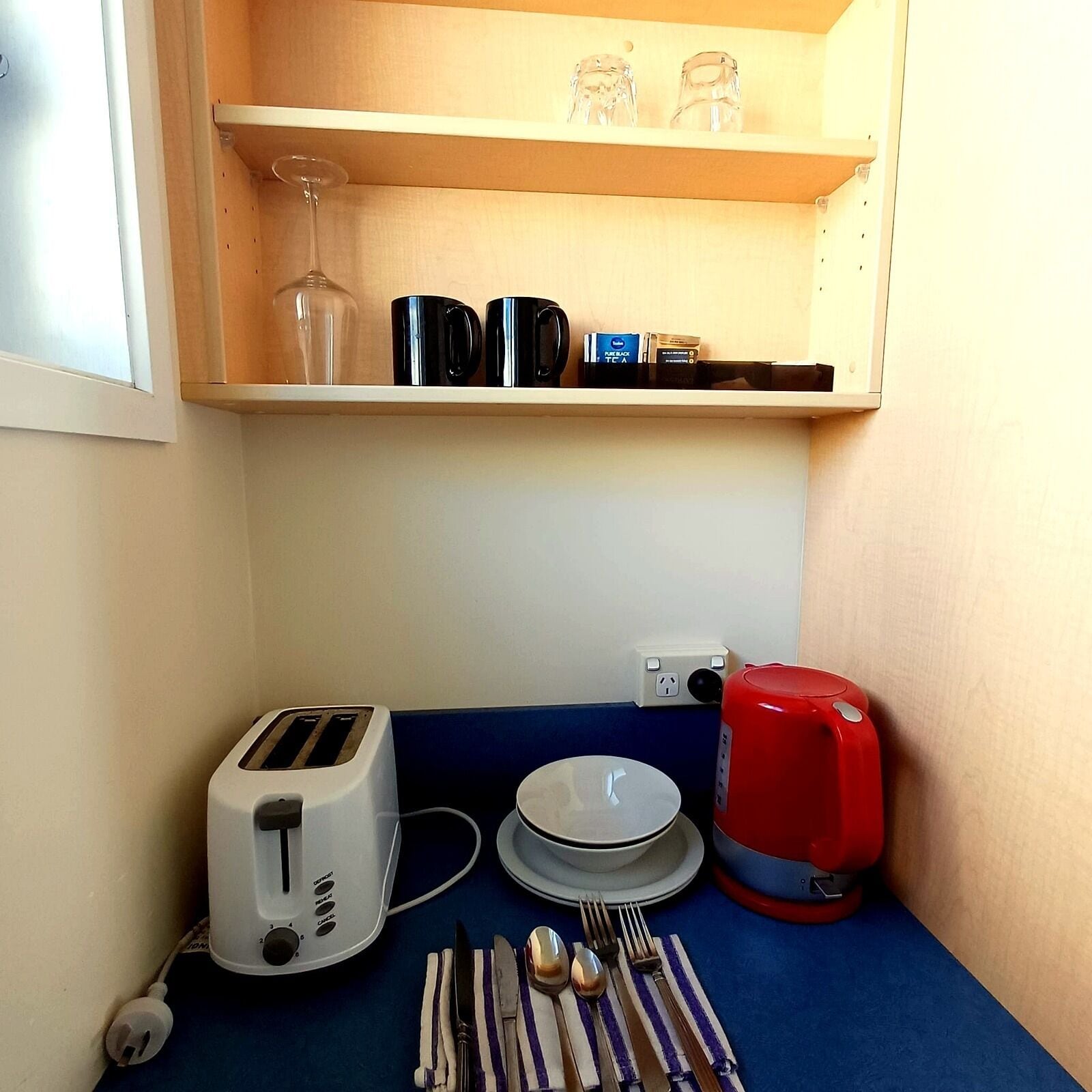 Una kitchenette con tostadora, hervidor, plato y cubiertos.