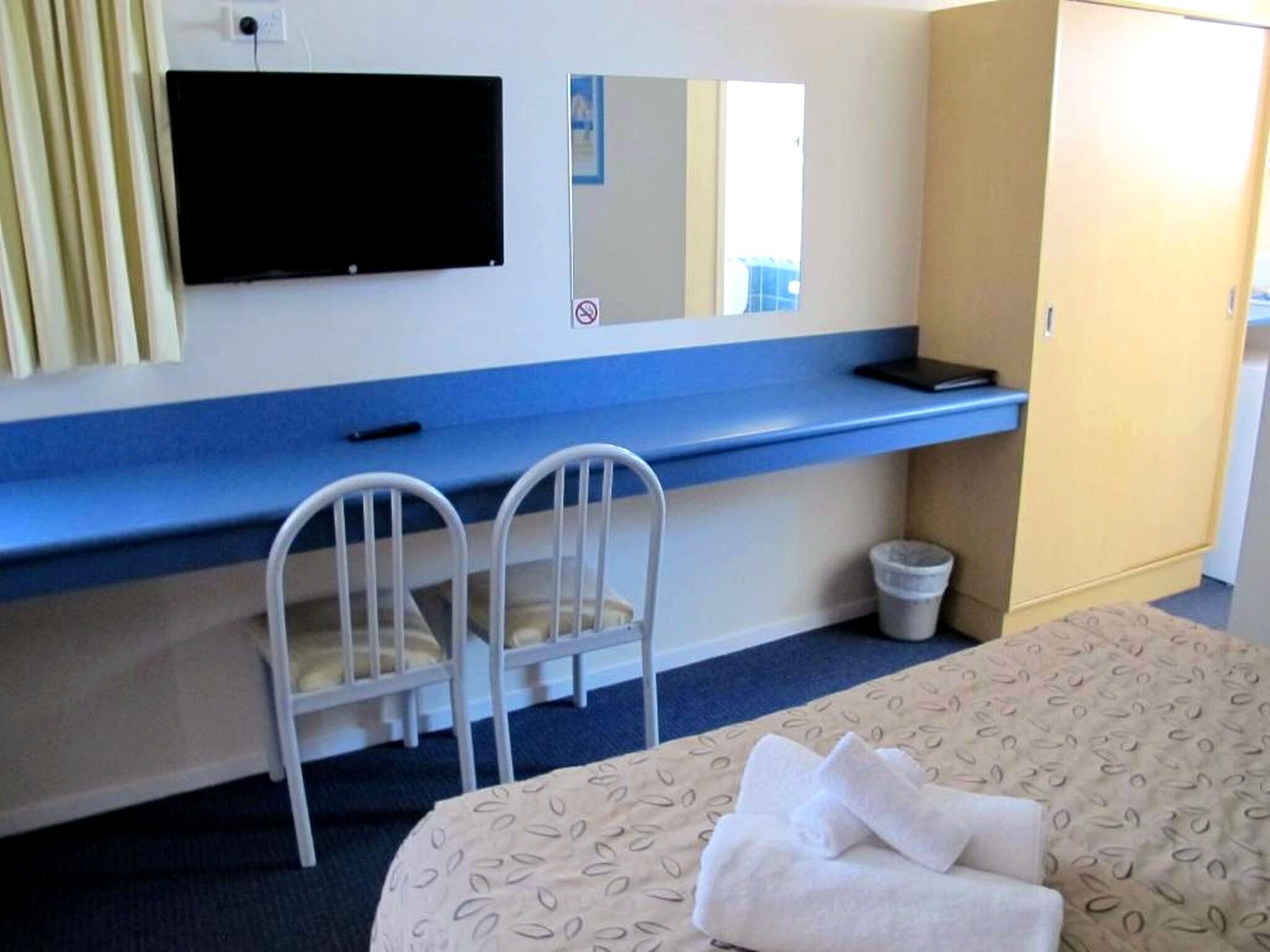 A hotel room with a bed, a desk with a chair, a television, and a wardrobe.