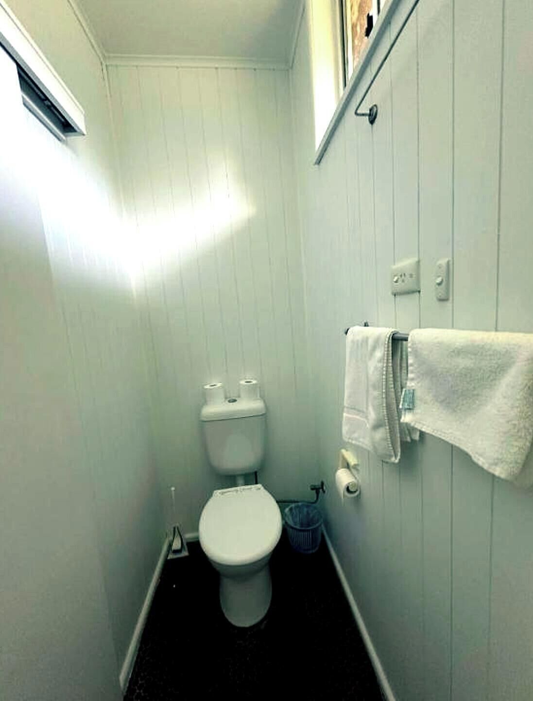 A small, narrow bathroom with a toilet, a trash bin, and a towel hanging on the wall.