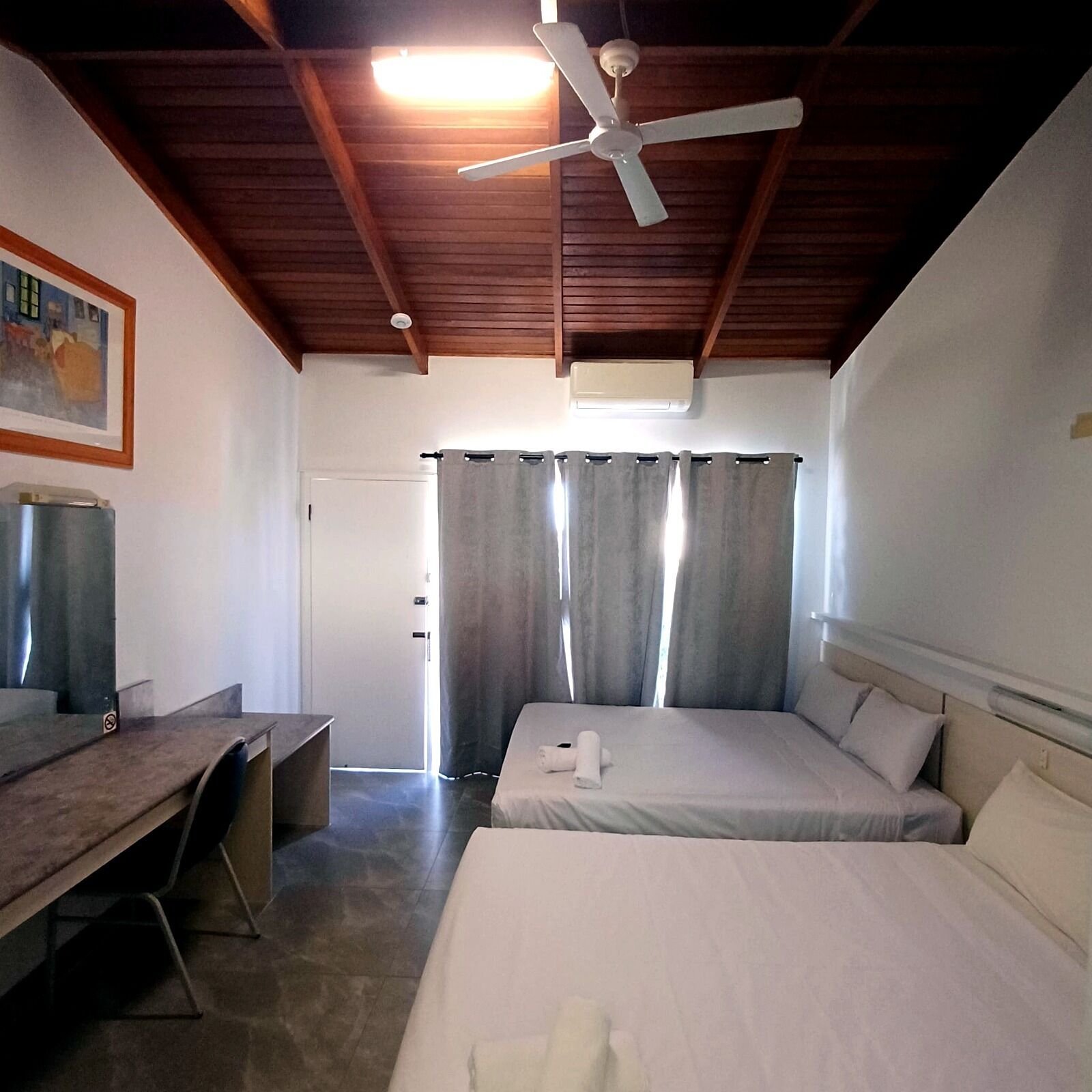 Un dormitorio con cama, escritorio, ventilador de techo y una puerta.
