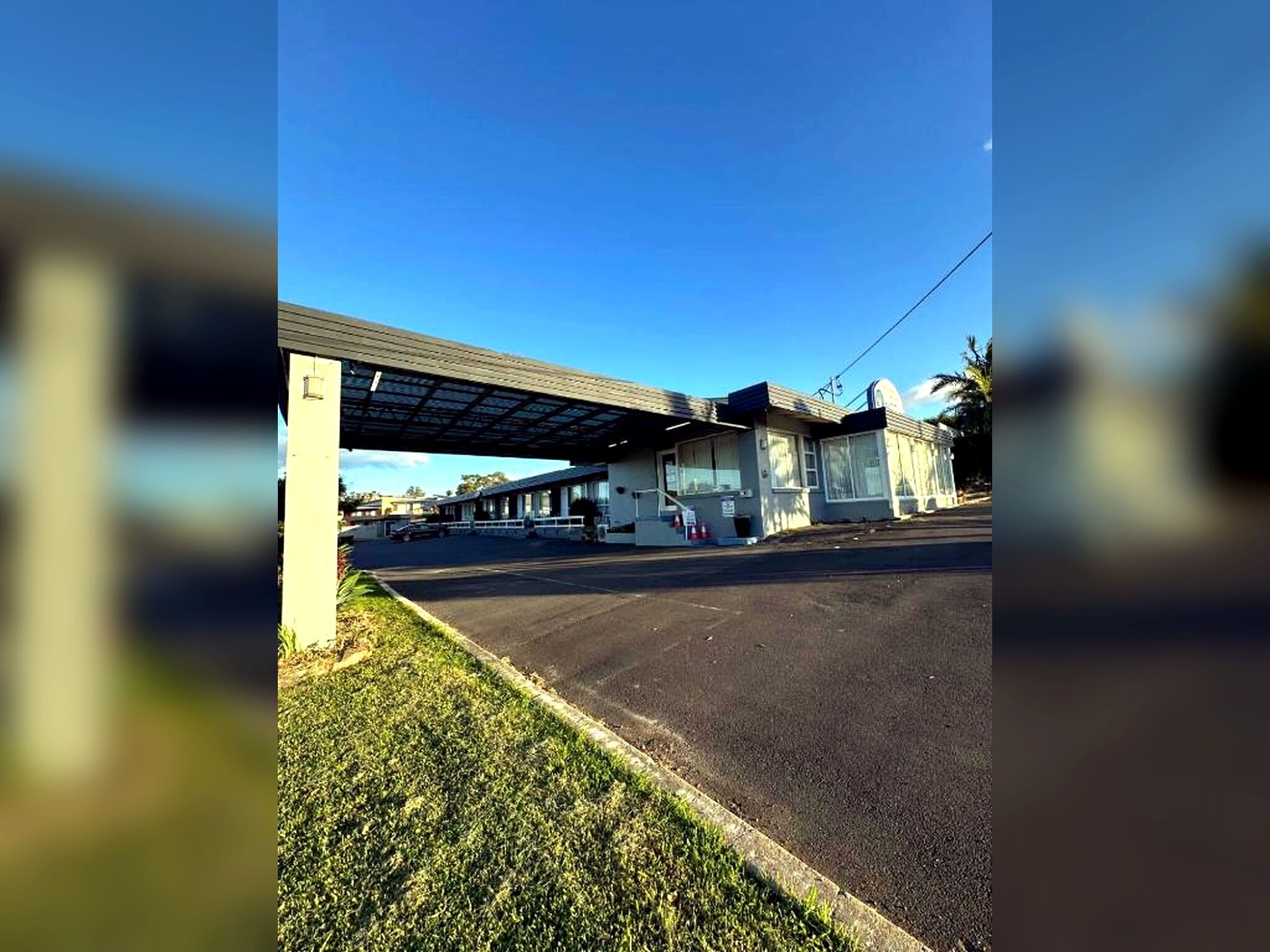 A motel with a covered parking area, a small building with a flat roof, and a clear sky.