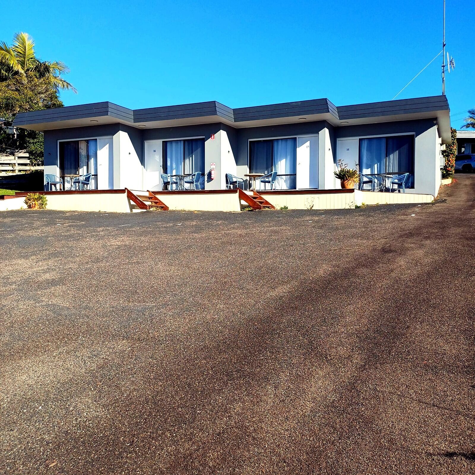 A motel with a flat roof, multiple rooms, and a small outdoor seating area with chairs and tables.