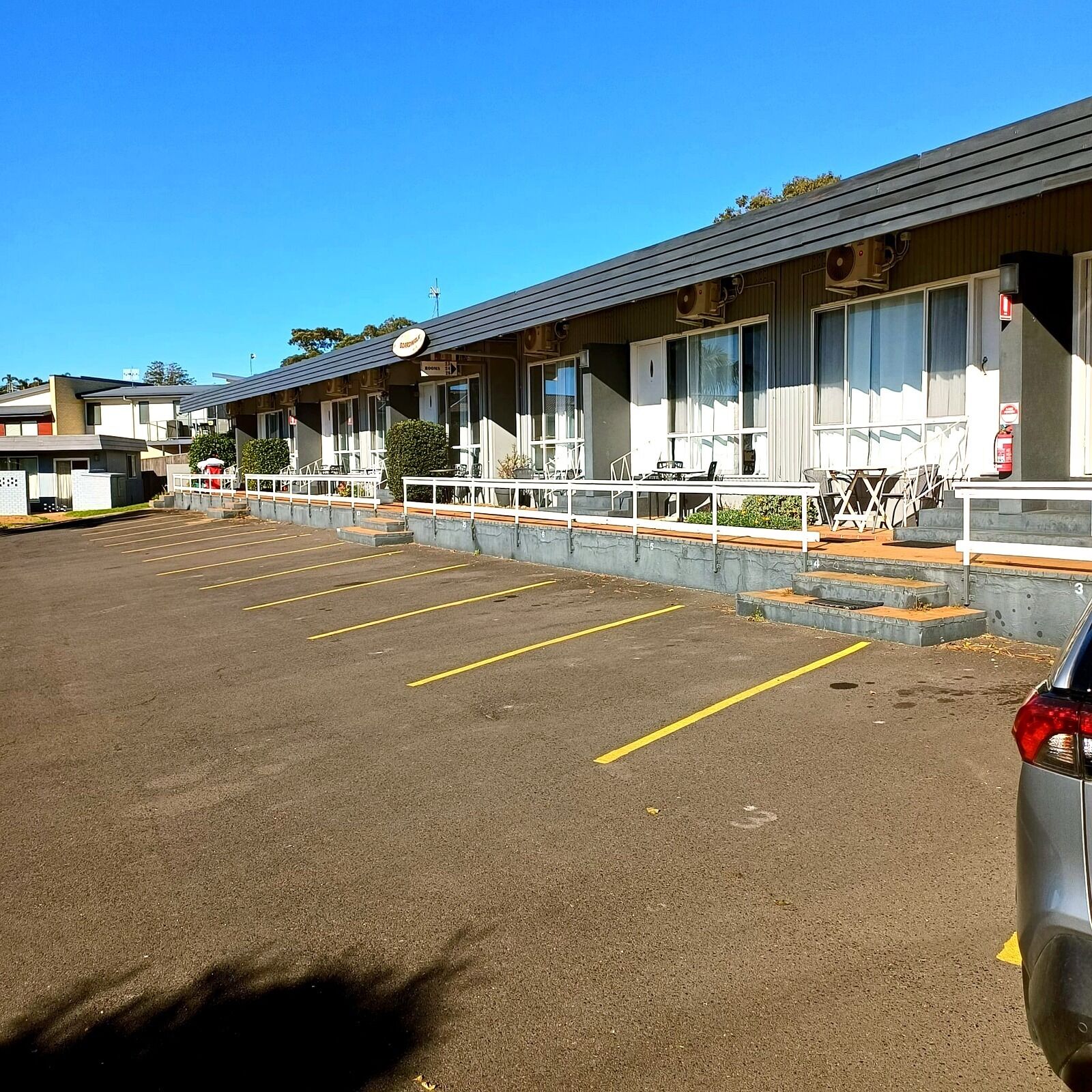 A motel with a parking lot, outdoor seating, and a fire extinguisher.