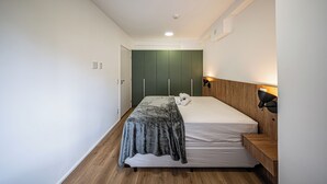Quarto com cama, chão de madeira, parede verde e mesa de cabeceira com abajur.